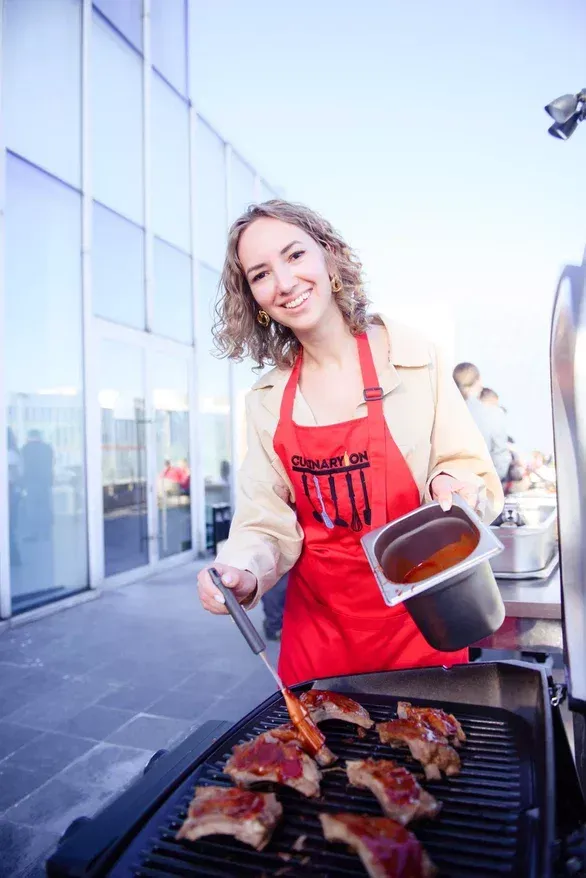 Участница поливает мясо соусом во время кулинарного тимбилдинга EventyOn