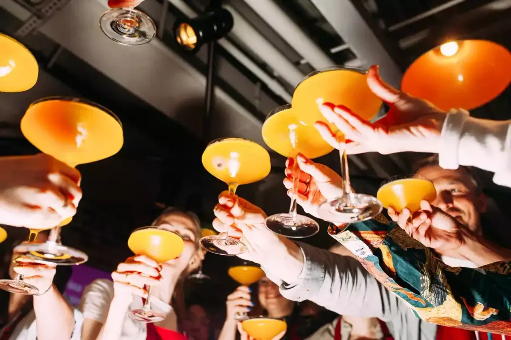 Гости поднимают бокалы с жёлтыми коктейлями вверх на вечеринке EventyOn