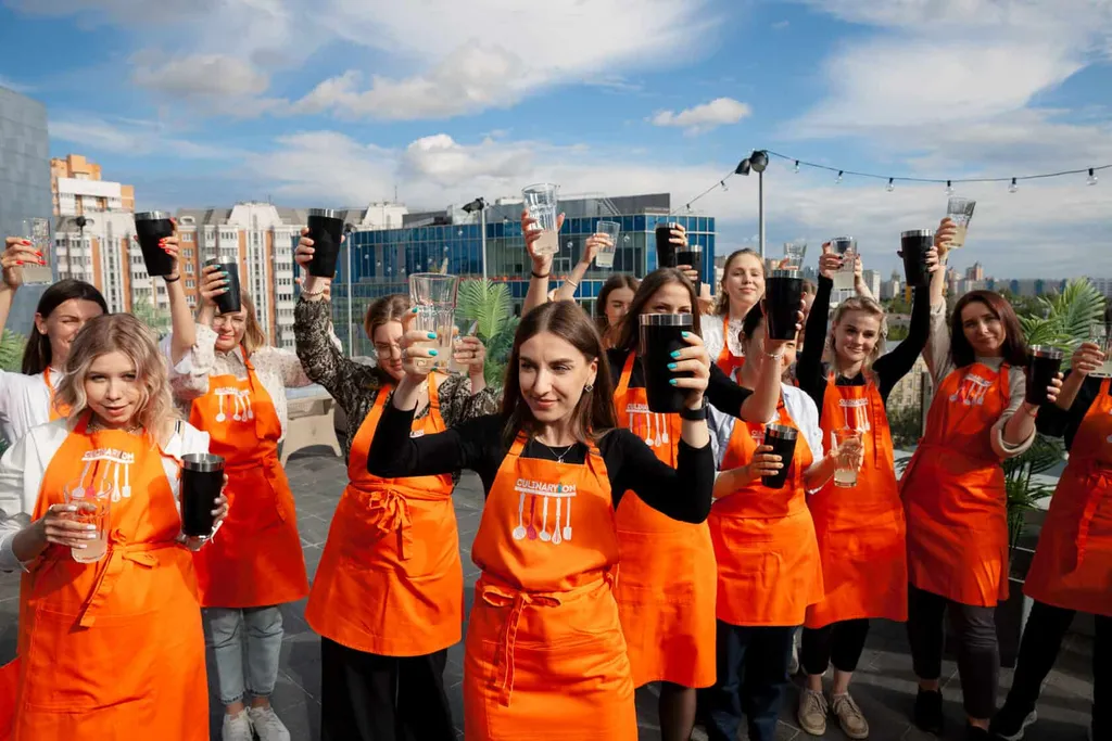 Участники в оранжевых фартуках CulinaryOn поднимают бокалы на открытой площадке во время коктейльного мероприятия